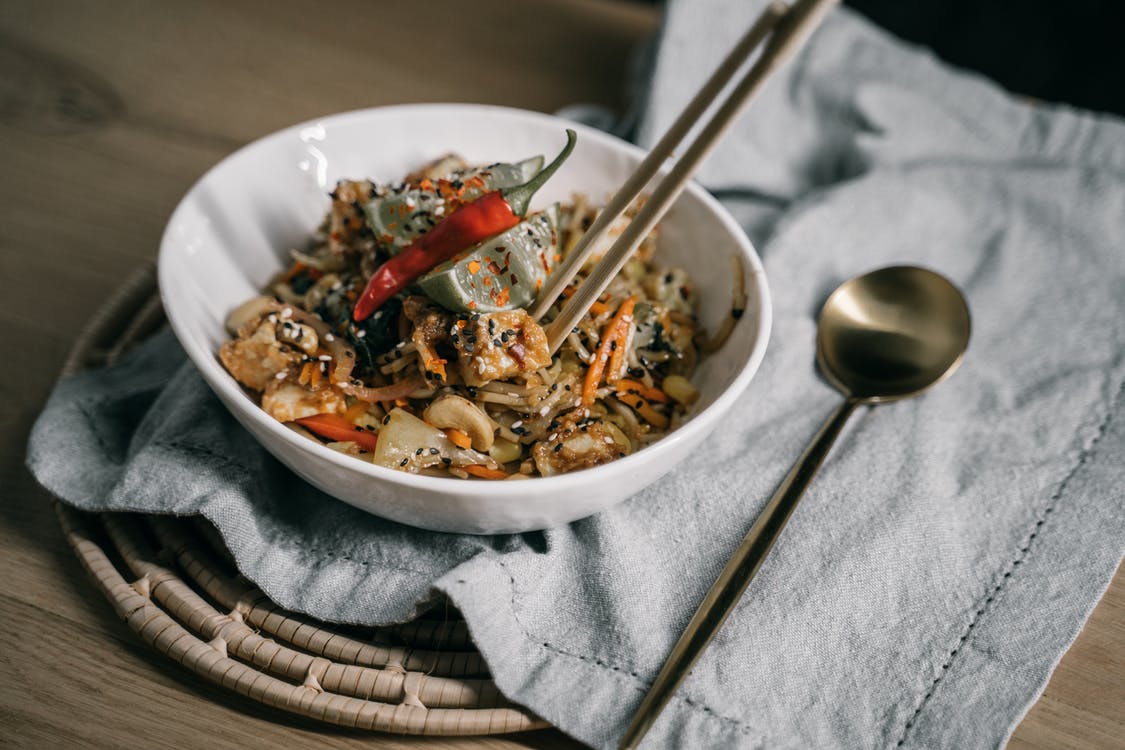 A spicy noodle dish on a table with chop sticks and a tasting spoon on the right