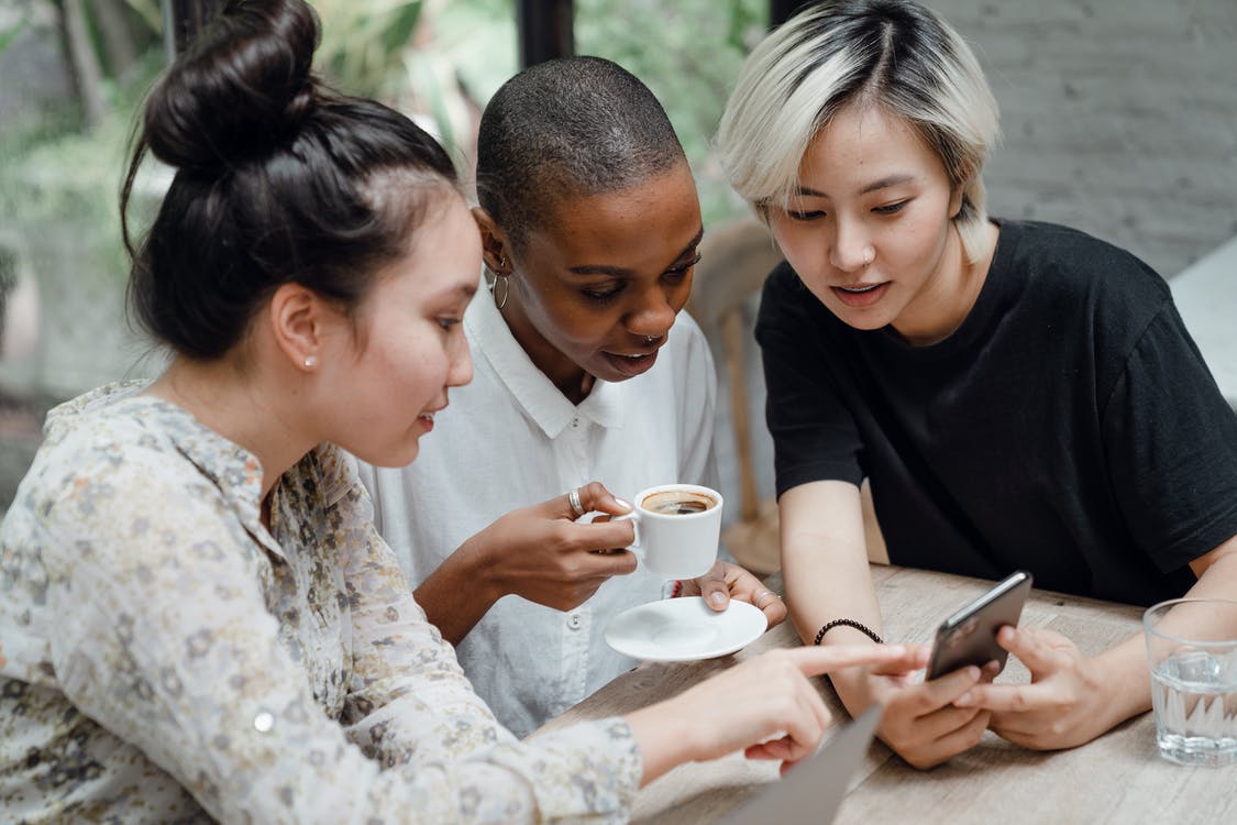 Three young women sitting down with them all looking at one ladys mobile phone