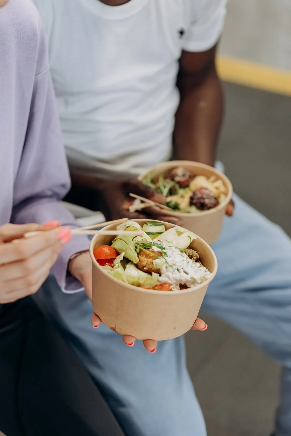 Two people eating out of a takeaway noodle cup with chopsticks